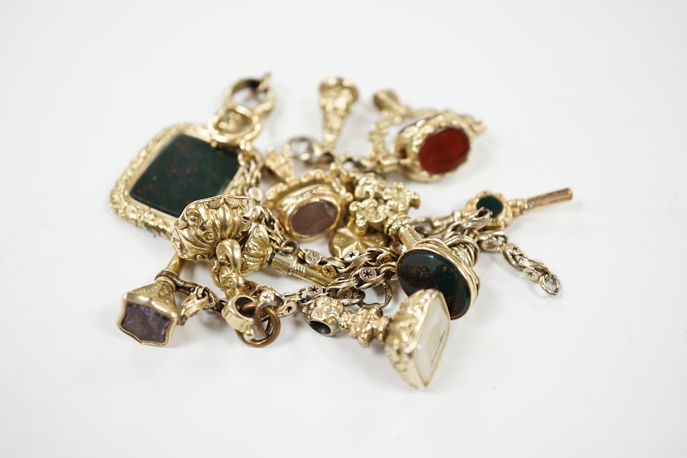 An early 20th century yellow metal charm bracelet (a.f.), hung with five assorted watch keys, together with seven assorted yellow metal overlaid and chalcedony set fobs.